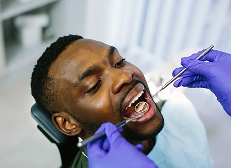 Man with black facial hair having dental exam by dentist in blue gloves