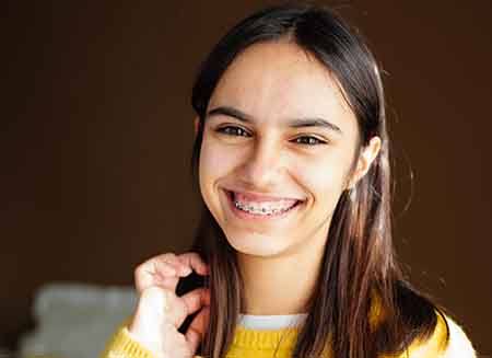 Woman in yellow sweater smiling with traditional braces