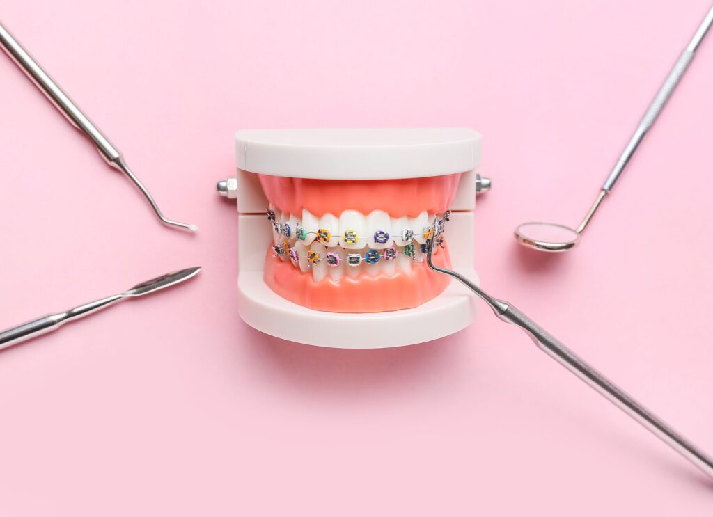 Braces on model teeth next to dental instruments with pink background